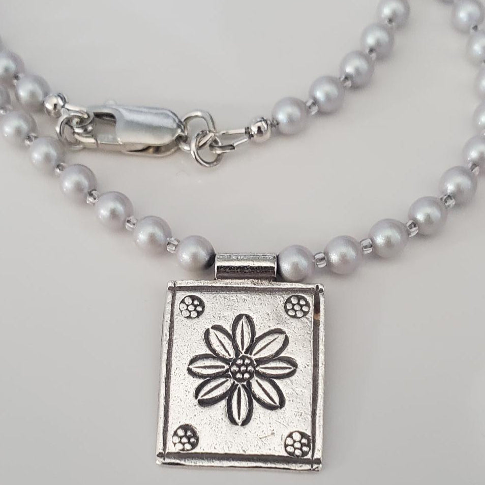 Pearl necklace with a silver pendant featuring a floral design on a light gray background