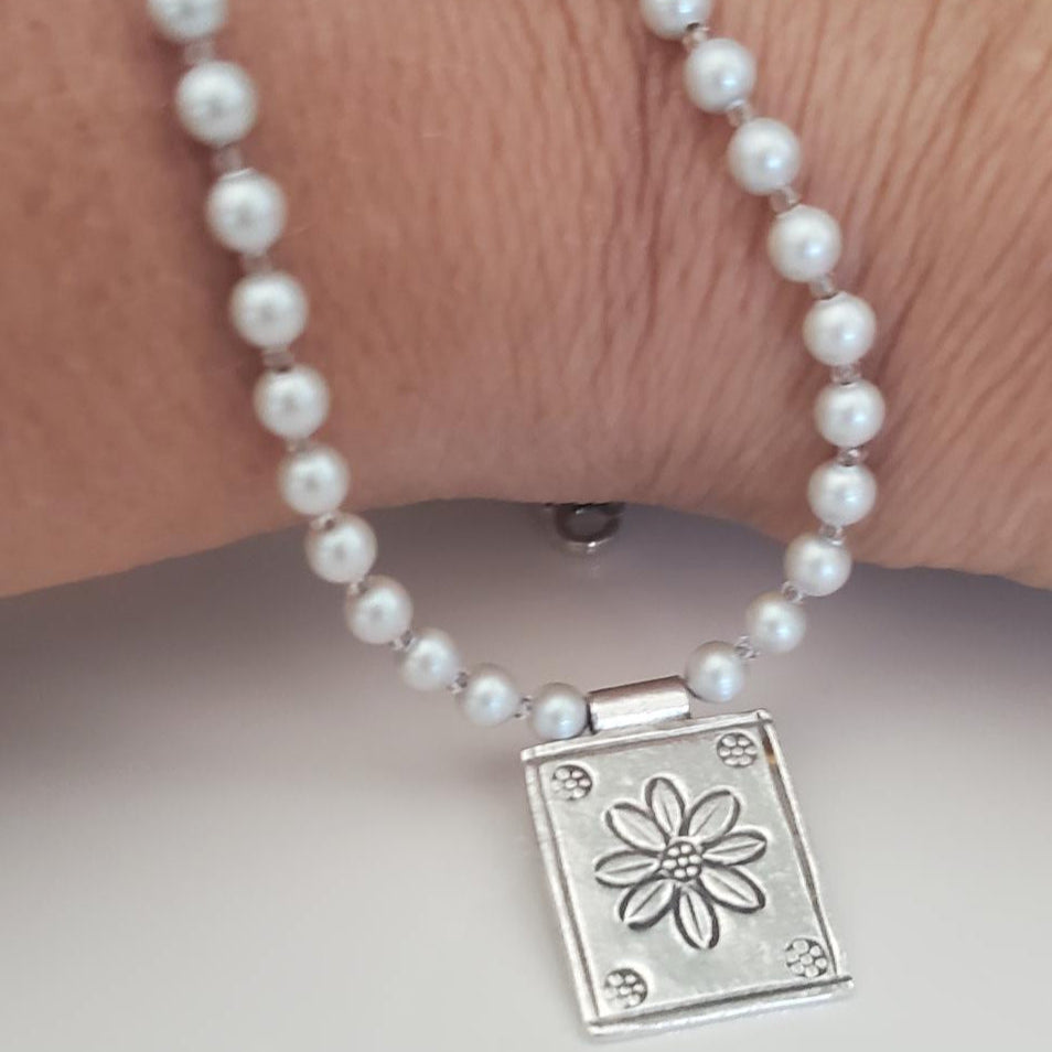 Pearl necklace with a silver clasp featuring a rectangle floral design pendant laying on writst