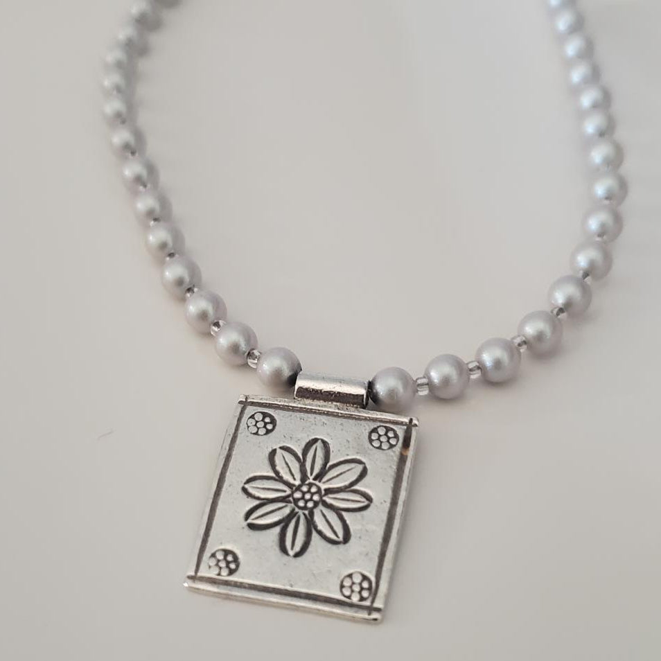 Gray swarovski pearl necklace with a square pendant featuring a flower design
