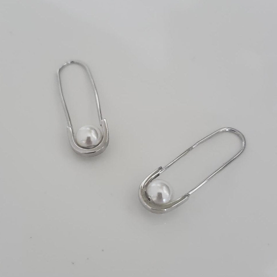 Two silver safety pins on a light gray background
