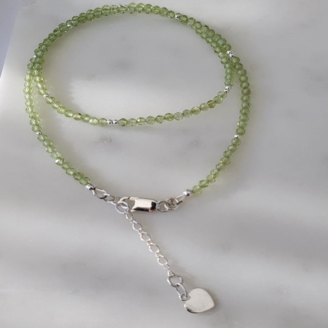 Picture of Peridot Gemstone Layering Necklace with Heart Charm. This necklace features 3.0mm micro-faceted peridot gemstones and a heart charm, symbolizing love and compassion. Its delicate design adds a touch of sophistication and elegance to any outfit, perfect for both formal and casual occasions.