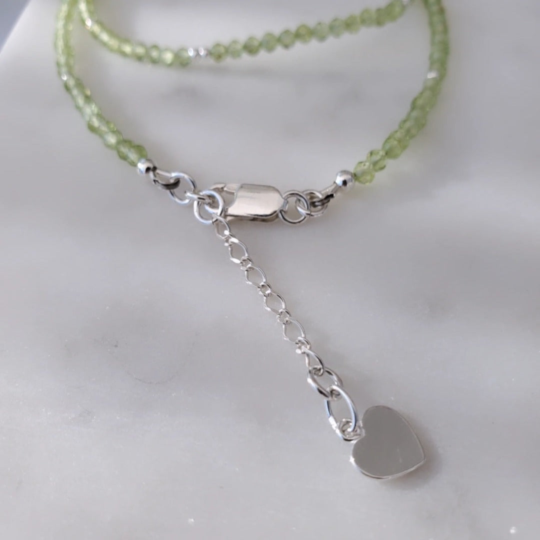Picture of Peridot Gemstone Layering Necklace with Heart Charm. This necklace features 3.0mm micro-faceted peridot gemstones and a heart charm, symbolizing love and compassion. Its delicate design adds a touch of sophistication and elegance to any outfit, perfect for both formal and casual occasions.