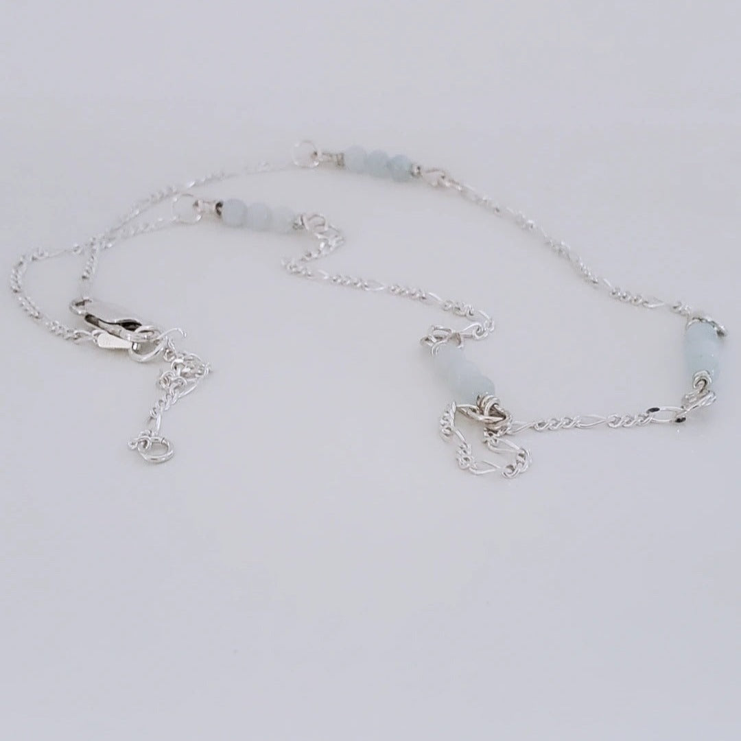 Picture of Aqua Serenity Sterling Silver Figaro Necklace. This necklace features a 2.2mm Modern Figaro style with genuine 4mm aquamarine gemstones interspersed in sets of three. Its minimalistic design exudes understated elegance, perfect for layering or wearing solo. Adjustable length of 17 inches plus a 2 inch extension allows for a customized fit.