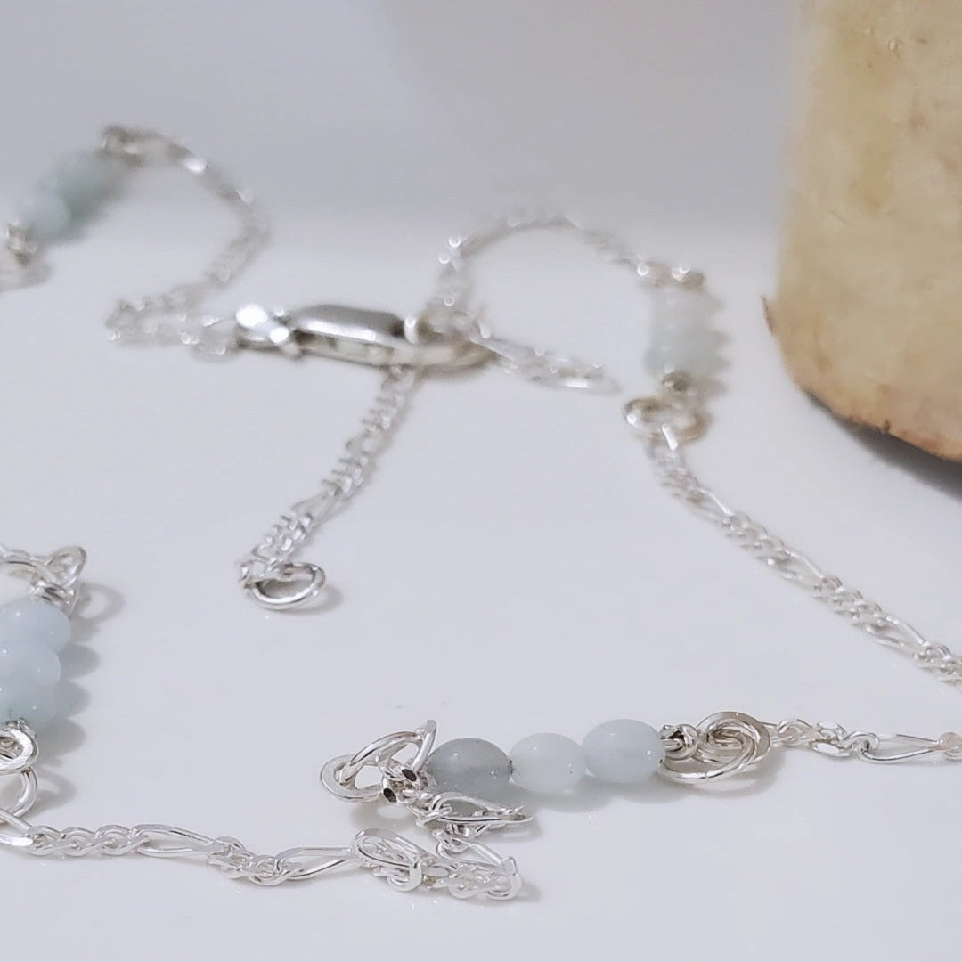Picture of Aqua Serenity Sterling Silver Figaro Necklace. This necklace features a 2.2mm Modern Figaro style with genuine 4mm aquamarine gemstones interspersed in sets of three. Its minimalistic design exudes understated elegance, perfect for layering or wearing solo. Adjustable length of 17 inches plus a 2 inch extension allows for a customized fit.