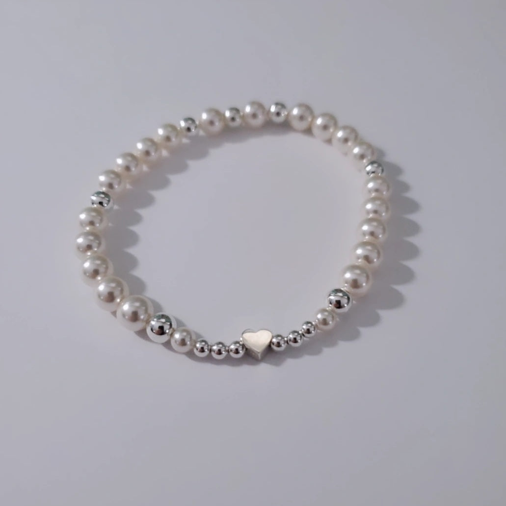Swarovski Pearl Harmony Heart Bracelet featuring a symphony of white Swarovski pearls and sterling silver beads, accented with a sweet heart charm. This bracelet embodies nature's melody, inviting harmony and joy. Crafted with passion and inspired by nature, it captures timeless elegance and the beauty of the natural world.