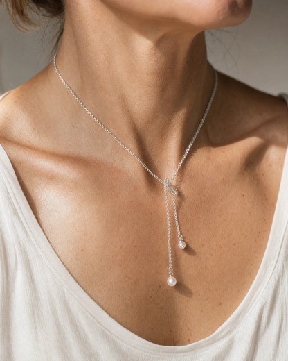 A close-up of a model wearing a delicate sterling silver pearl lariat necklace , paired with a white top.
