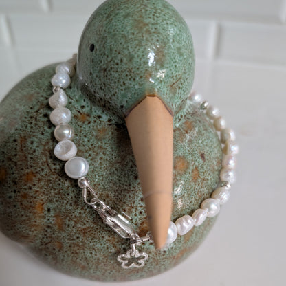 A green speckled ceramic duck-shaped jewelry stand holding a white pearl bracelet with a silver clasp and flower charm, set against a white tiled background.