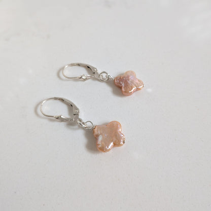 A pair of silver leverback earrings with small, irregularly shaped peach-pink beads, displayed on a light gray surface.