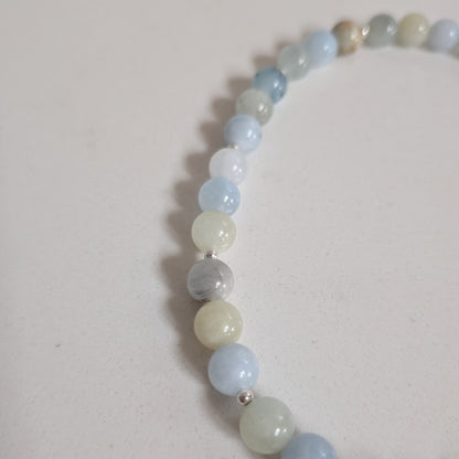 A beaded stretch bracelet made of smooth, polished round gemstone beads in light blue, pale green, white, and gray, with small silver spacer beads, shown on a neutral off-white background.