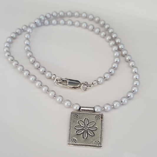 Pearl necklace with a silver clasp featuring a floral design on a white background