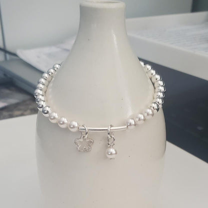 Silver bracelet with a daisy and pearl charms on a white vase against a blurred background