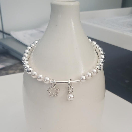 Silver bracelet with a daisy and pearl charms on a white vase against a blurred background