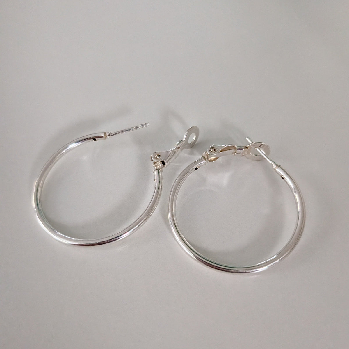 A pair of large, thin silver hoop earrings with simple post-back closures, displayed on a neutral light gray background.