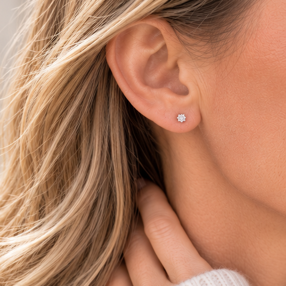 A close-up of a woman's ear wearing a small 3mm crystal cubic zirconia stud earring. The earring is set in a sterling silver and is shown on a model with blonde hair.