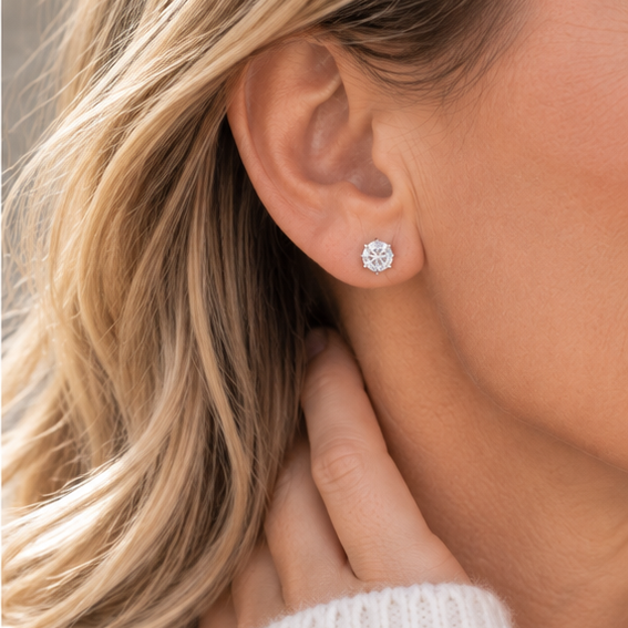 A close-up of a woman's ear wearing a 5mm crystal cubic zirconia stud earring, with her hand resting near her neck and blonde hair visible.