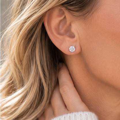 A close-up of a woman's ear wearing a 5mm crystal cubic zirconia stud earring, with her hand resting near her neck and blonde hair visible.