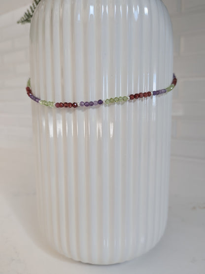 A delicate beaded bracelet with multicolored round beads, wrapped around a white ribbed ceramic vase.