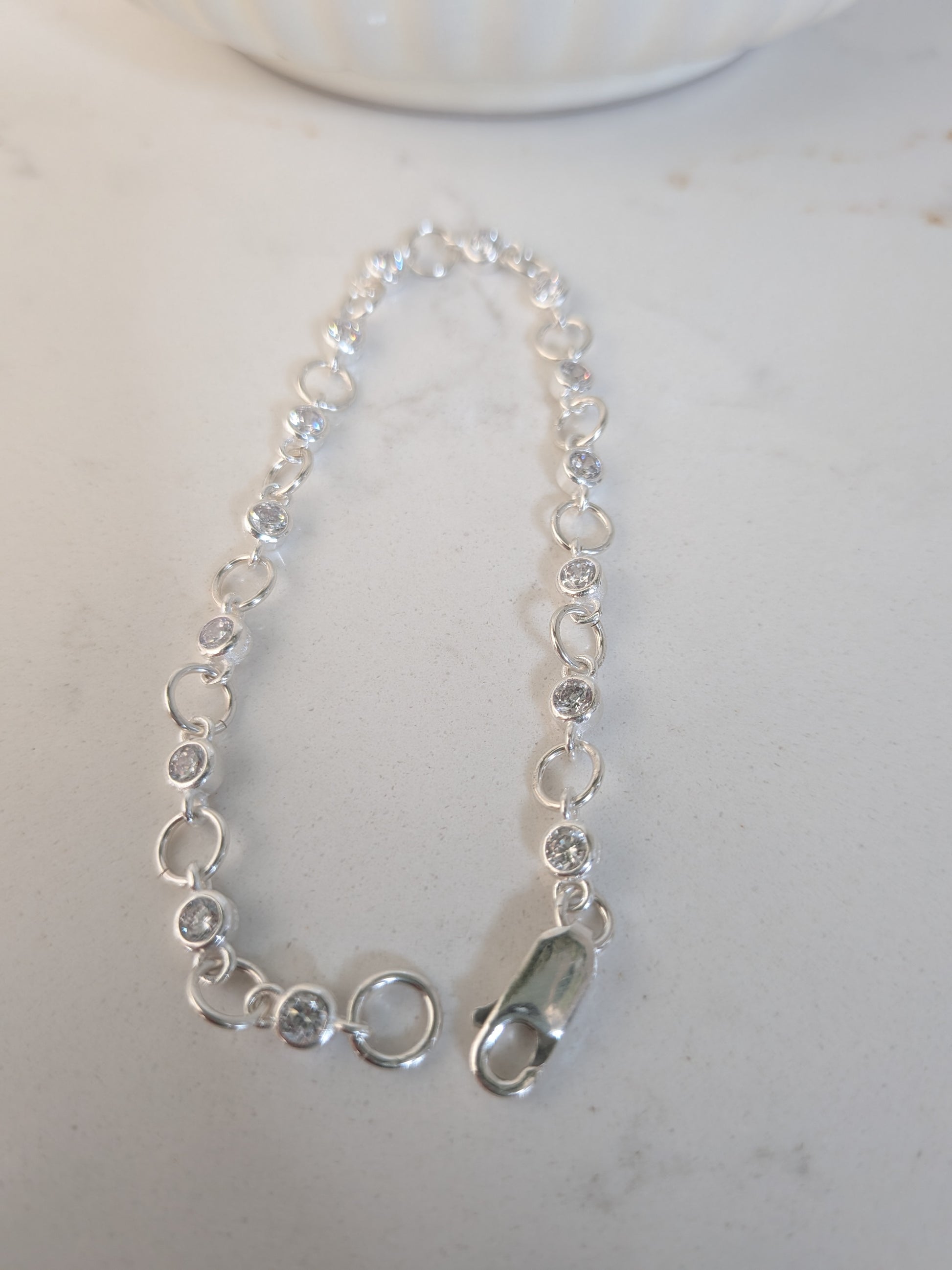 A delicate silver chain bracelet with small circular links and a lobster clasp, displayed on a light-colored surface.