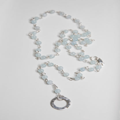 Picture of the handmade Sterling Silver Aquamarine Necklace "BELIEVE." This 31" necklace features genuine aquamarine round gemstones linked with 20g sterling silver, secured with a lobster clasp. The washer-style pendant stamped with "BELIEVE" adds a meaningful touch, symbolizing authenticity, growth, love, inspiration, education, integrity, and joy. Wear it as a regular necklace or transform it into a lariat style to accentuate your style and remind yourself of these powerful principles.