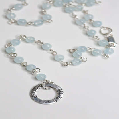 Picture of the handmade Sterling Silver Aquamarine Necklace "BELIEVE." This 31" necklace features genuine aquamarine round gemstones linked with 20g sterling silver, secured with a lobster clasp. The washer-style pendant stamped with "BELIEVE" adds a meaningful touch, symbolizing authenticity, growth, love, inspiration, education, integrity, and joy. Wear it as a regular necklace or transform it into a lariat style to accentuate your style and remind yourself of these powerful principles.