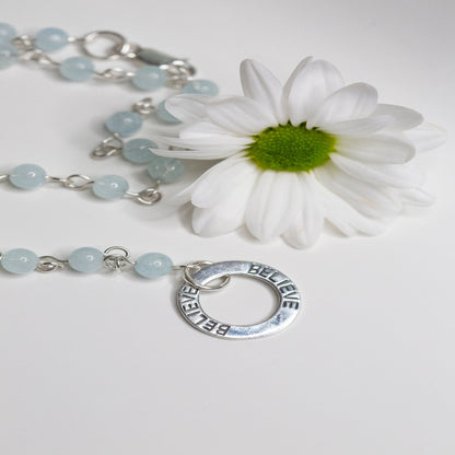 Picture of the handmade Sterling Silver Aquamarine Necklace "BELIEVE." This 31" necklace features genuine aquamarine round gemstones linked with 20g sterling silver, secured with a lobster clasp. The washer-style pendant stamped with "BELIEVE" adds a meaningful touch, symbolizing authenticity, growth, love, inspiration, education, integrity, and joy. Wear it as a regular necklace or transform it into a lariat style to accentuate your style and remind yourself of these powerful principles.