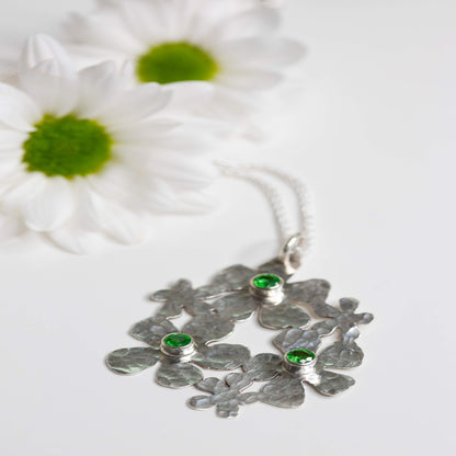 Image of a Sterling Silver Handmade Daisy Delight Necklace adorned with vibrant tsavorite garnets. This stunning piece features a 20-gauge sterling silver pendant, tube-set tsavorite garnets, and a sterling silver wheat chain with a lobster clasp. Inspired by nature, the delicate daisy cluster design and captivating gemstones evoke a sense of beauty and transformation, perfect for reconnecting with nature's allure and awakening the beauty within.