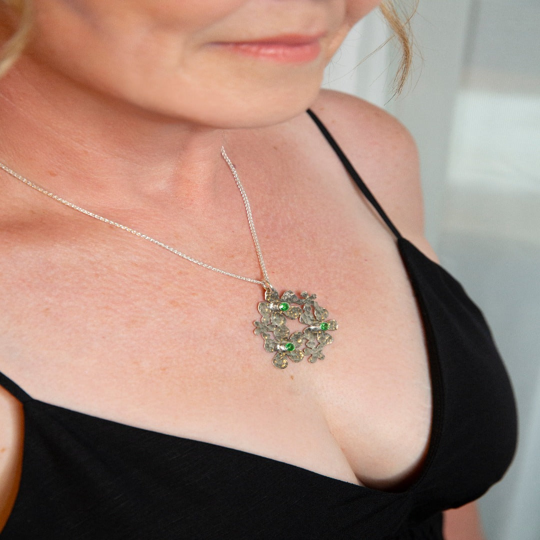 Image of a Sterling Silver Handmade Daisy Delight Necklace adorned with vibrant tsavorite garnets. This stunning piece features a 20-gauge sterling silver pendant, tube-set tsavorite garnets, and a sterling silver wheat chain with a lobster clasp. Inspired by nature, the delicate daisy cluster design and captivating gemstones evoke a sense of beauty and transformation, perfect for reconnecting with nature's allure and awakening the beauty within.