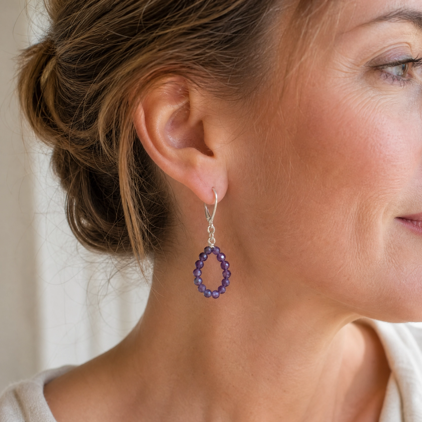 A close-up of a woman wearing a dangling hoop earring made of small purple stones in a silver setting.