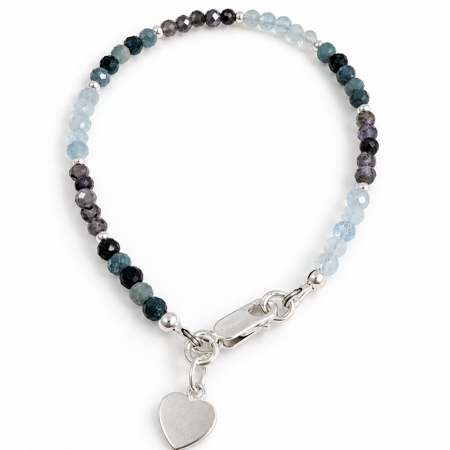 A beaded bracelet featuring faceted beads in light blue, dark bluel, and charcoal purple/gray, finished with a polished silver lobster clasp and a dangling heart charm, set against a plain white background.