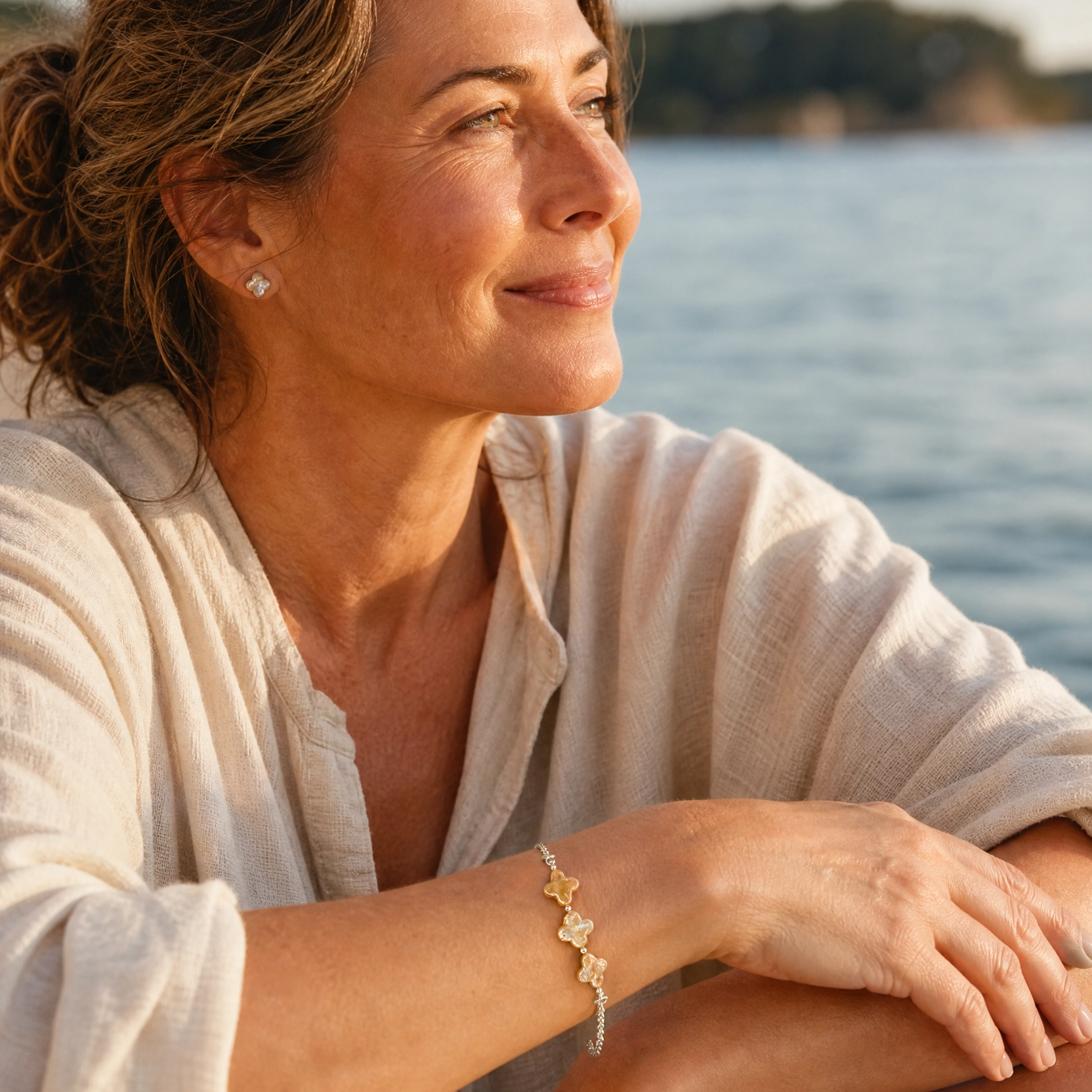 A woman sitting outdoors by the water wearing a delicate silver rolo chain bracelet with champagne four leaf clover pearls.