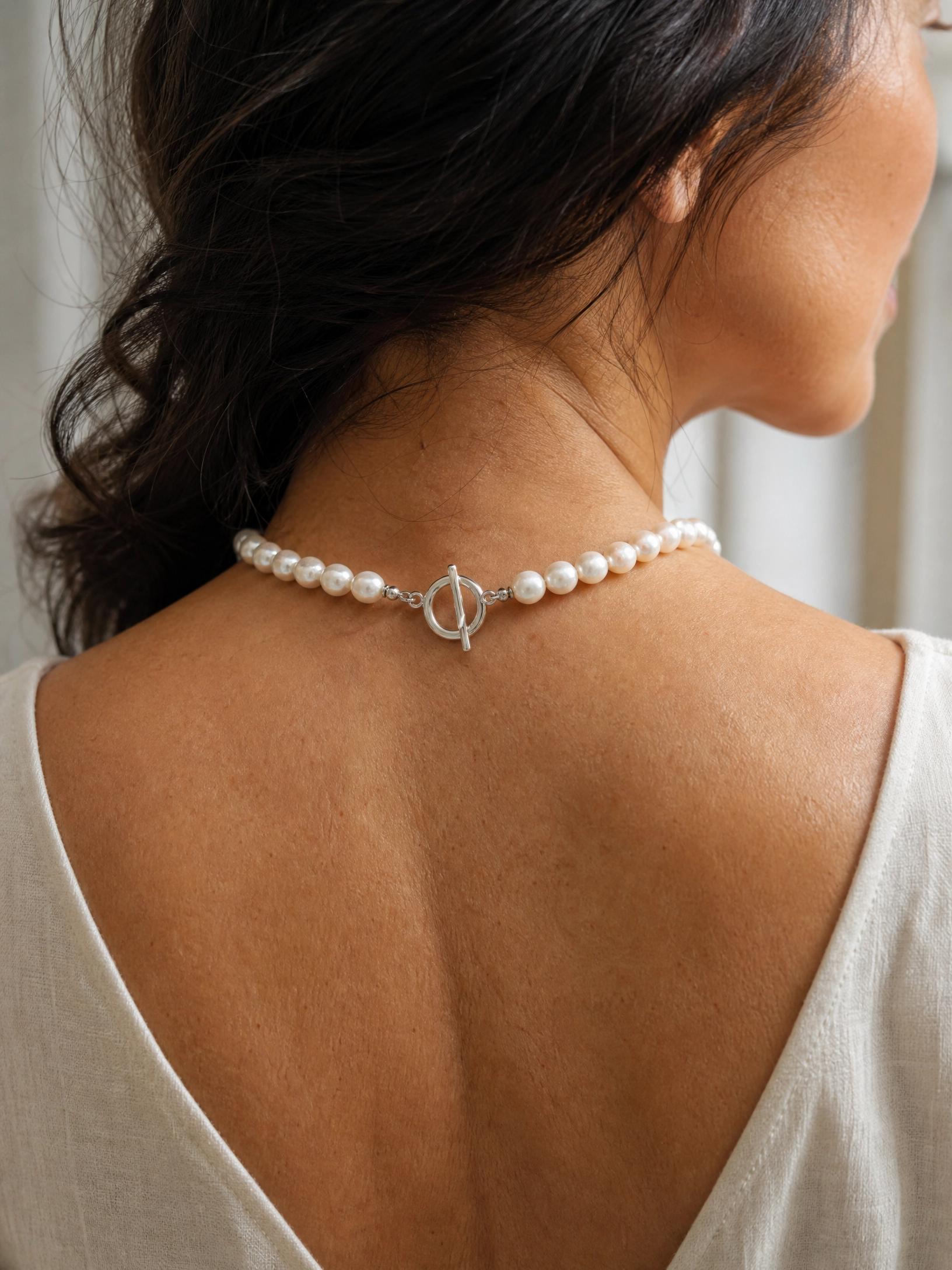 A close-up back view of a woman wearing a pearl choker necklace with a silver toggle clasp.
