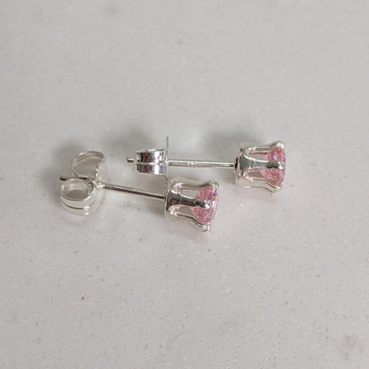 A pair of silver stud earrings with small pink faceted gemstones, displayed on a light gray textured surface.