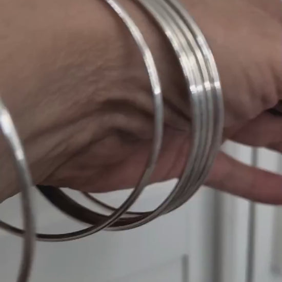 Sterling silver bangles shown layered on women's wrist with movement.