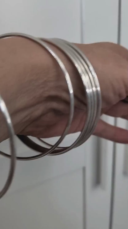 Sterling silver bangles shown layered on women's wrist with movement.