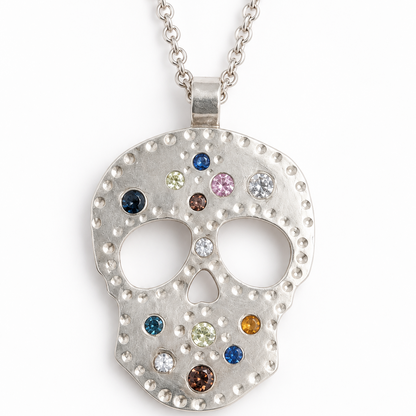 A silver skull pendant necklace adorned with small, colorful gemstones, suspended from a silver chain against a plain white background.